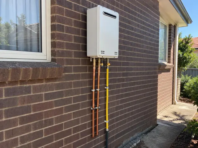 Wall-mounted hot water unit with copper and yellow pipework on a brick house exterior in Auburn