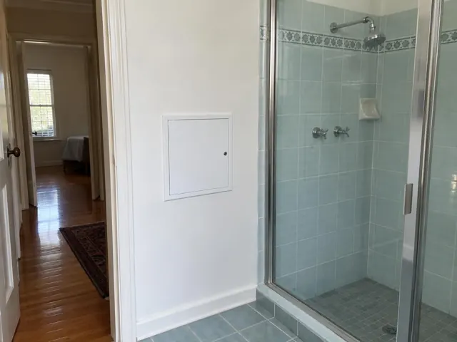 Bathroom shower wall with a small access panel beside tiled shower in a home in Berala